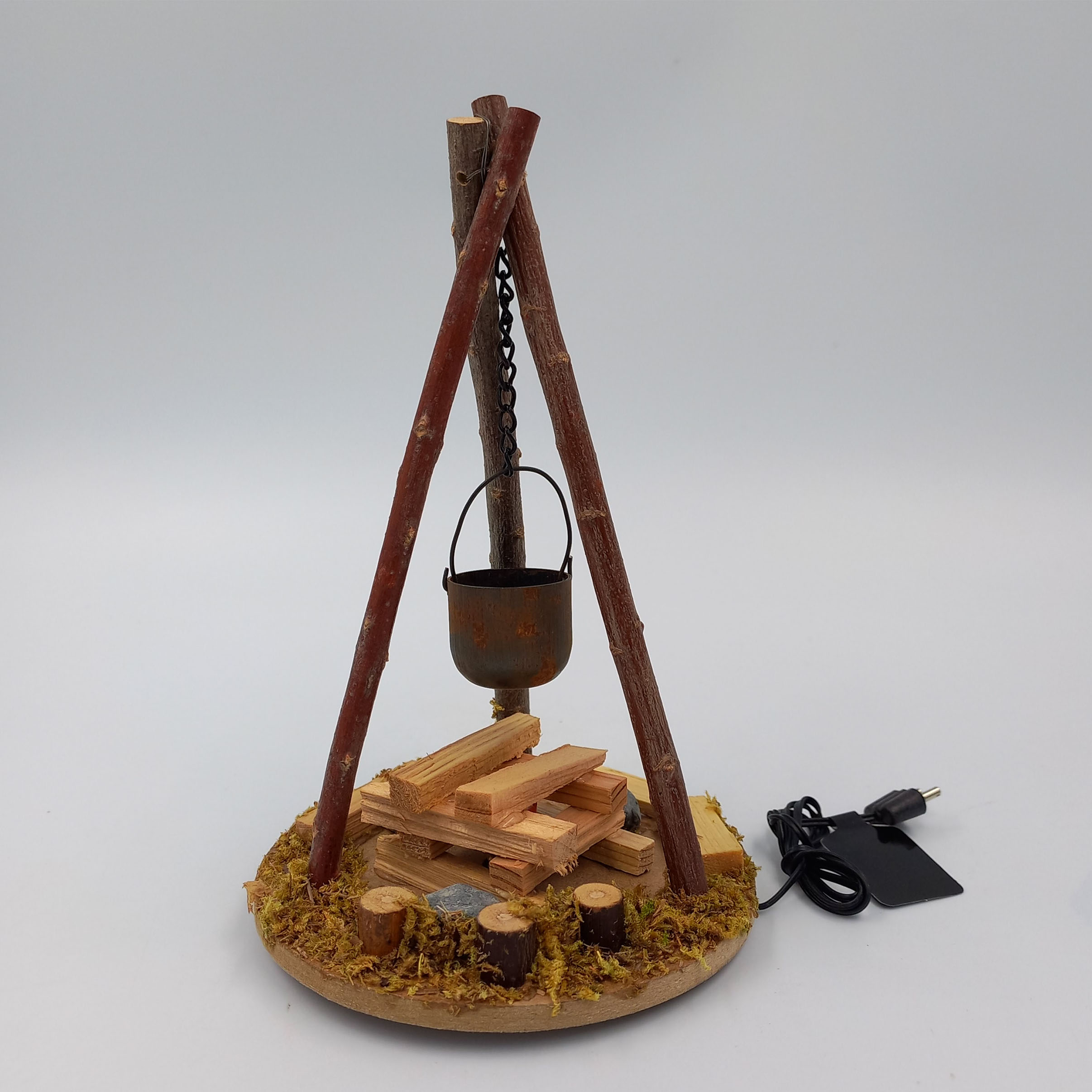 Kübel an Dreibock über Feuer hängend neben Baumstamm